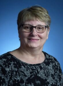 A woman with glasses and short hair wearing a black shirt.